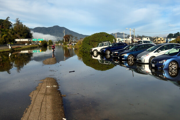 A flooded bike path between a California highway and a parking area