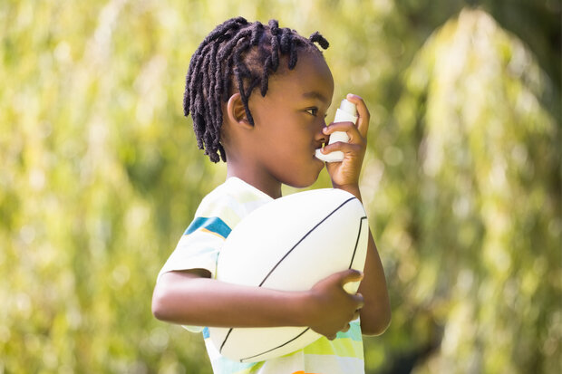 Young boy holding a football and using an inhaler