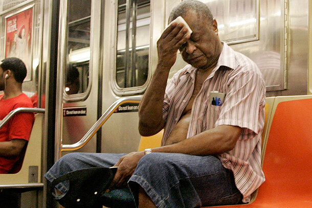 A man wearing his shirt unbuttoned wipes sweat off his forehead with a hankerchief